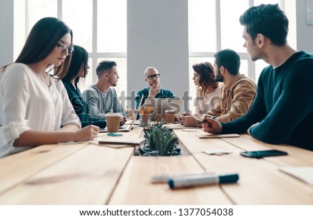 Staff meeting. Group of young modern people in smart casual wear discussing something while working in the creative office          