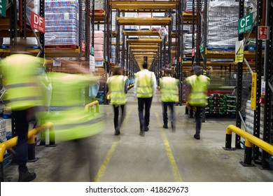 Staff In Reflective Vests Walking In A Warehouse, Back View