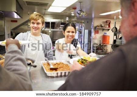Staff Serving Food In Homeless Shelter Kitchen