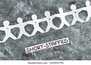 staff shortages and business struggling after the pandemic conceptual image, paper people chain with question marks on some workers and Short-staffed text on black background - Shutterstock ID 2192957793