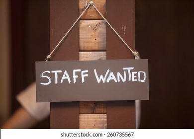 Staff wanted inscription on a board hanging on wooden post.