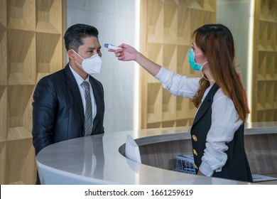 Staff  woman wear protective masks  at the counter used the digital thermometer to measure the temperature of visitors at the building.Measures to prevent people with fever, Covid 19 concept. - Shutterstock ID 1661259619