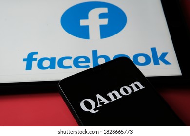 Stafford / UK - October 7 2020: QAnon Vs FACEBOOK. QAnon Organisation Logo Seen On The Smartphone Which Is Placed On Tablet With Facebook Logos On It. Concept For Ban Of QAnon On Social Media. 