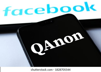 Stafford / UK - October 7 2020: QAnon Organisation Logo Seen On The Smartphone. Blurred Tablet With Facebook Logos On The Background. Concept For Ban Of QAnon On Social Media. 