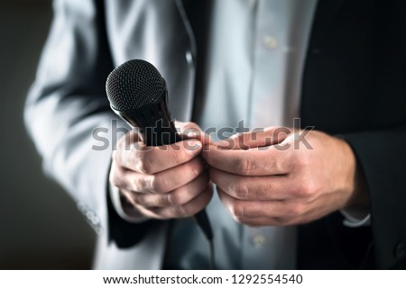 Stage fright concept. Nervous and shy public speaker with microphone. Business man afraid of giving speech for crowd of people or audience. Sweaty hands holding mic. Bad presentation. Stressed singer.