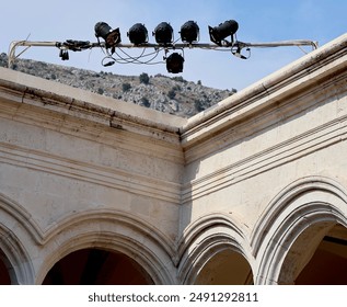 Stage lighting setup on a historical building with arched details and a mountainous backdrop