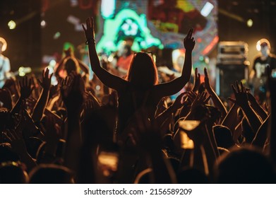 Stage lights against woman with with arms raised while enjoying a concert on a music festival. Crowd with raised hands.