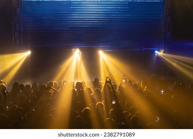 Stage lights creating a dramatic concert atmosphere - a lot of people with phone looking to shoe and waiting