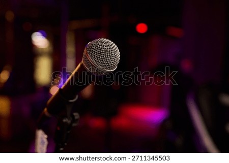Stage microphone close-up ready for performance with shallow bokeh background, textured grille catching warm stage LEDs and blurred band equipment suggesting