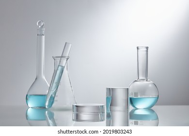 Stage showcase cosmetics on glass pedestal modern in laboratory equipment. Laboratory glass equipment with blue water ingredients on white background. Research and development cosmetics concept