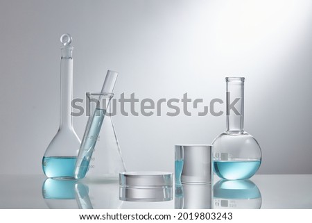 Stage showcase cosmetics on glass pedestal modern in laboratory equipment. Laboratory glass equipment with blue water ingredients on white background. Research and development cosmetics concept