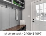 A staged detail shot of a gray mudroom entryway with bench seating, coat hooks, and storage above. A scarf hangs from a hook and a plant sitting on a shelf.