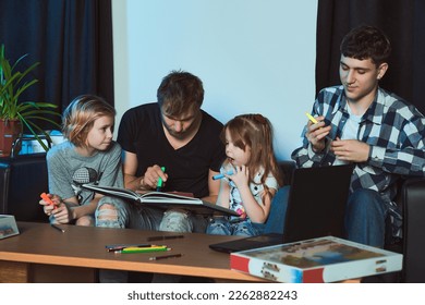 Staged photo  Homosexual couple   their children  two cute girls  at home    All are sitting together   picking up markers  Perhaps they are going to draw in notebook                            
