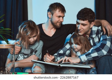   Staged photo  Homosexual couple   their children  two cute girls  at home  Everyone is sitting side by side together  One the boys is finishing drawing in his notebook  You're so good at it! 