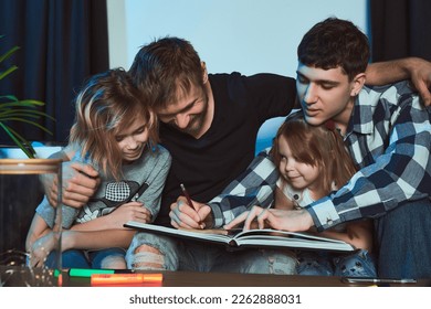 Staged photo  Homosexual couple   their children  two cute girls  at home  One the boys is finishing drawing in his notebook  The other is hugging him   the older girl                        