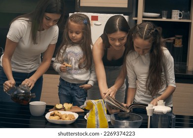    Staged photo. Lesbian couple and their children in the kitchen. Everyone takes part in cooking a delicious meal. First you have to choose the right recipe.                            