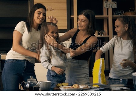  Staged photo. Lesbian couple and their children in the kitchen. The kids are the main chefs. You can draw with flour! Mom laughs and paints the face of the younger girl with flour.                   