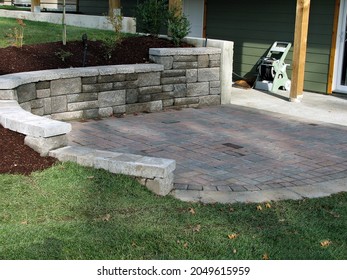 staggered block retaining wall with small paving stone patio deck surrounded by grass area and planted area - Shutterstock ID 2049615959
