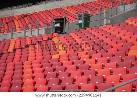 Staggered rows of empty red stadium seats, with refuse bins on landing