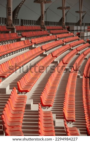 Staggered sections of seating in stadium, red plastic box seats mounted to concrete