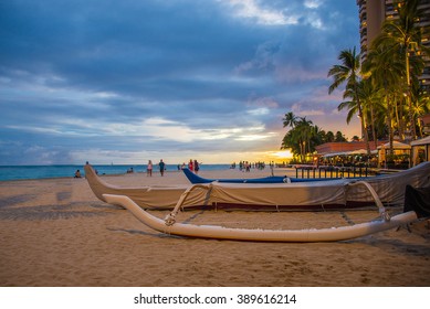 Staggering sunset view from the Waikiki beach with blue skies and a traditional sailing boat docked at the shore.