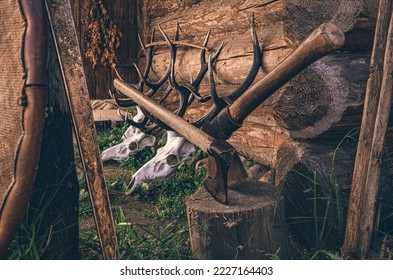 A stag's skull and antlers along with an ax and block of wood in front of a wooden hut. Skulls and axes surreal decoration in open air museum. - Powered by Shutterstock