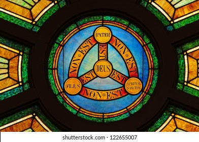 Stained Glass Window Depicting Doctrine Of The Holy Trinity In Latin With Symbols Of Circle And Triangle