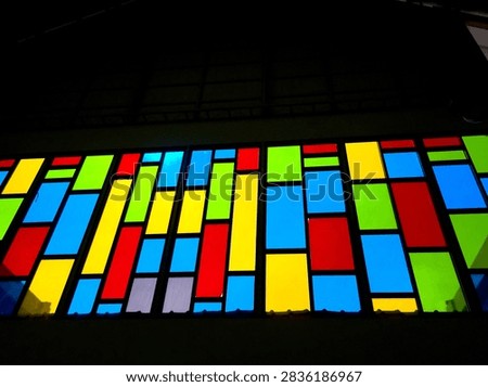 A stained glass window with a grid of rectangular panels in red, blue, yellow, green, and light blue