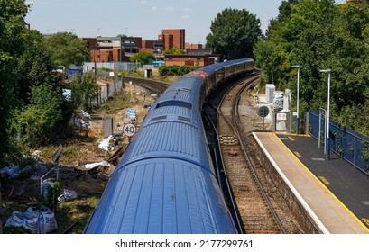 Staines-upon-Thames, UK  July 11th 2022  A Commuter Train Bound For Windsor Departs From Staines Railway Station. South West Trains. Tracks, Rail Junction, Town Centre Trees. From High Angle