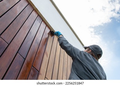 Staining the wood facade cladding with paint brush and protective oil, stain, house improvement copy space, looking up perspective angle - Shutterstock ID 2256251847