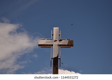 stainless cross placed on a romania church with a partially cloudy sky behind it