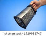 Stainless metal kitchen grater with plastic handle held in hand by Caucasian male hand studio shot isolated on blue background.