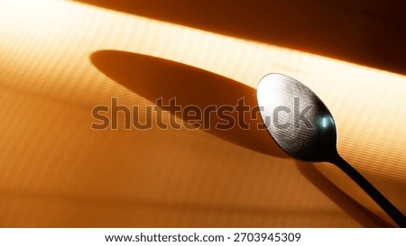 Stainless spoon placed at the angle with diagonal shadow reflection during summer. Close-up spoon and ray of light texture. Still-life, abstract, kitchenware, minimal concept for background, print.
