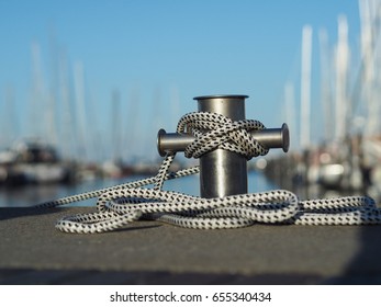 Stainless steel bollard with rope in a luxury marina, soft bokeh with luxury boats and yachts