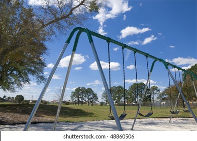 Stainless Steel Childrens Swing Set With Partly Cloudy Blue Sky And Southern Oak Tree Near By