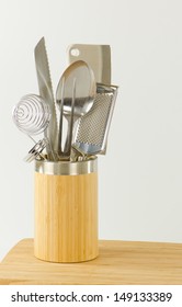 Stainless Steel Cooking Utensils In A Bamboo Container On A Wooden Cutting Board