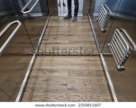 stainless steel elevator cabin interior with hardwood oak floor and mirror paneling. handrail and reclining seat for seniors and relaxation in luxury offices, wood, wooden