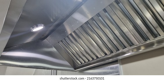 Stainless steel exhaust hood showing shining grease filters and lights in a commercial kitchen - Shutterstock ID 2163750101