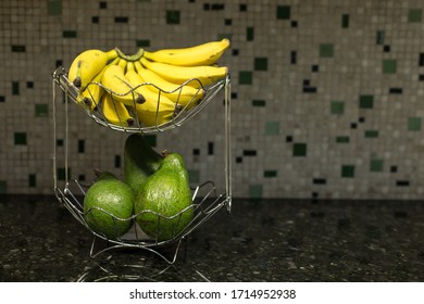 Stainless Steel Fruit Bowl With Avocados And Bunch Of Bananas On Kitchen Counter With Textured Background