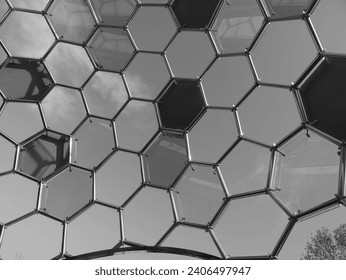 A stainless steel and glass structure with a hexagonal pattern, looking up towards the sky. The structure is large and imposing, and it dominates the surrounding landscape. The sky is blue and cloudle - Powered by Shutterstock