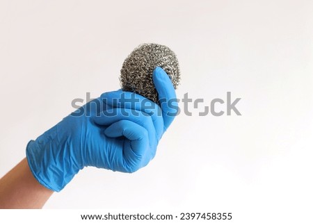 Stainless steel kitchen brush. Barbecue cleaning tools. A hand in a latex blue glove holds a stainless steel ball brush. Dishwashing brush, kitchen tool, light background