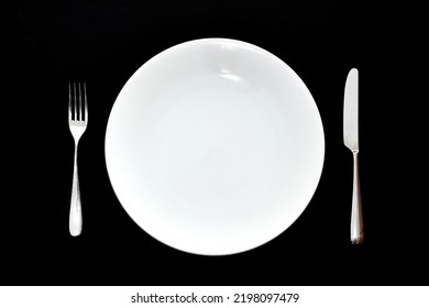 Stainless Steel Knife And Fork And Empty White Dinner Plate On A Plain Back Background. No People.