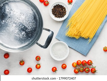 Stainless Steel Metal Cooking Pot Of Boiling Water With Raw Spaghetti Ingredients For Cooking Pasta, Tomato, Pepper, Salt, Top View On Concrete Background, Flat Lay