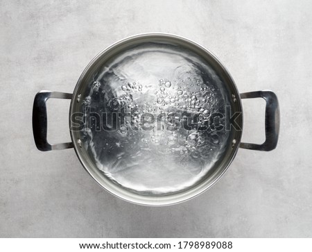 Stainless steel metal cooking pot of boiling water on gray concrete background , top view. 