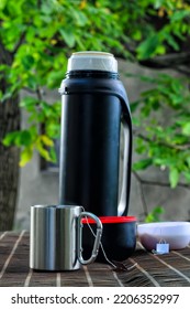 Stainless Steel Mug With Tea Bag, Black Thermos With Two Bowls, Walnut Tree With Green Leaves In The Background, Autumn Mood, Cold Weather, Selective Focus On The Mug