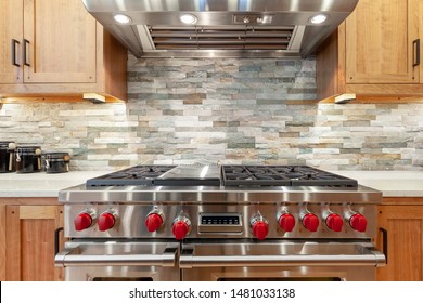 Stainless Steel Oven And Stove With Red Knobs, Stainless Steel Hood, Brown Kitchen Cabinets, Slate Mosaic Backsplash, Natural Stone, Black Jars