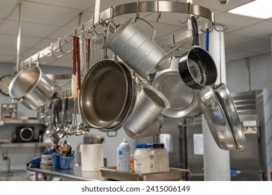 Stainless steel pots and pans and other cooking utensils hanging in a commercial industrial kitchen.  - Powered by Shutterstock