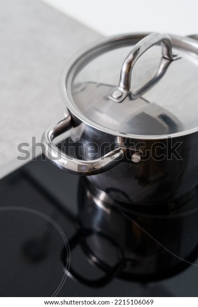 stainless steel saucepan with handle and lid on glass\
ceramic stove at contemporary kitchen, cooking food on cooker\
hob