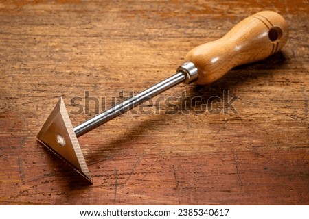 stainless steel shave hook scraper with wooden handle against grunge wood