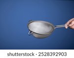 Stainless steel sieve. Held by hand by Caucasian male hand. Close up studio shot, isolated on blue.